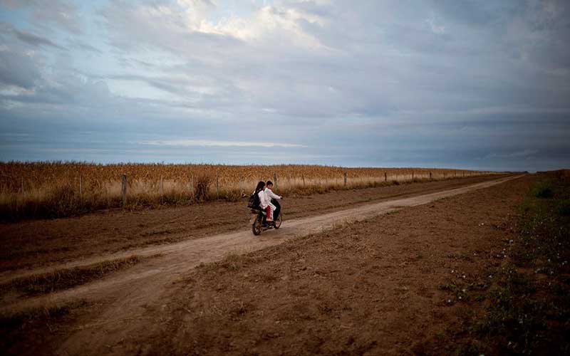 students-ride-a-motorbike-past-a-field-of-biotech-corn-on-their-way-to-school-in-Pozo-del-Toba